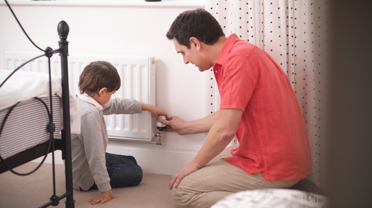 Man helping young boy adjust radiator in a bedroom